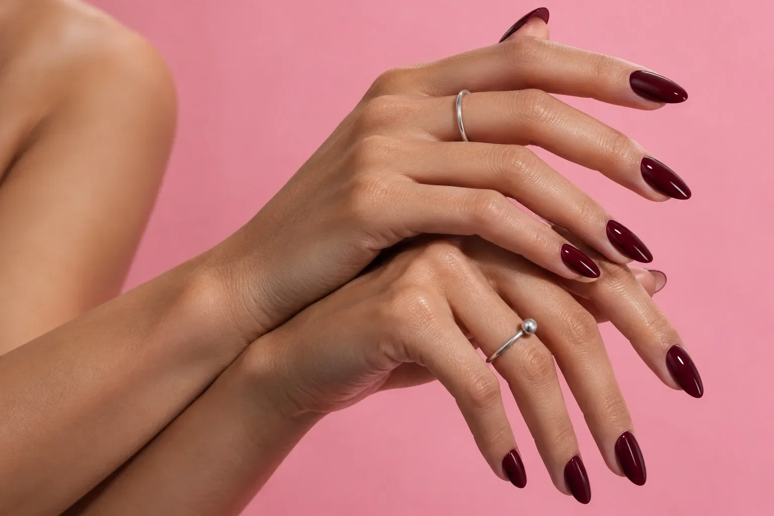 Illustrative editorial hands with glossy burgundy nails against pink